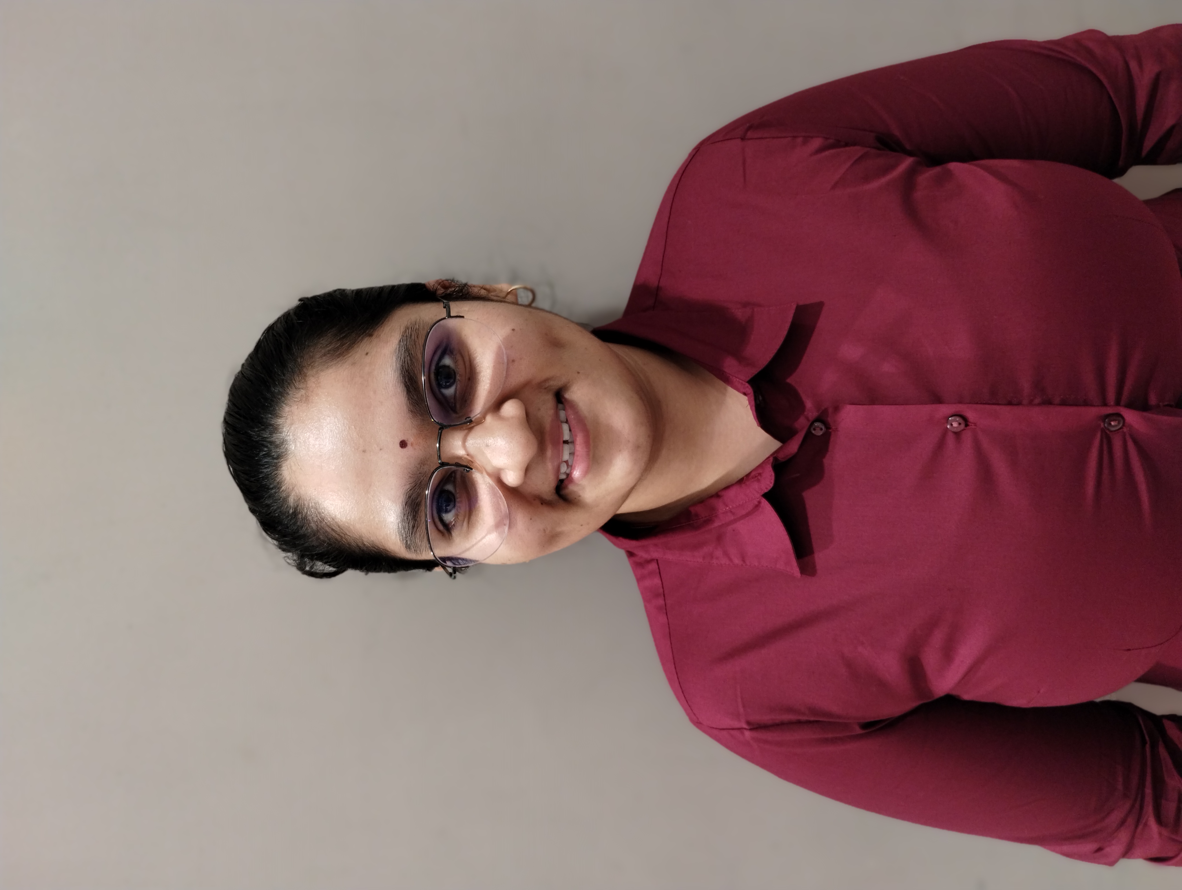 Supriya M smiling in a red plaid shirt and tortoise shell glasses